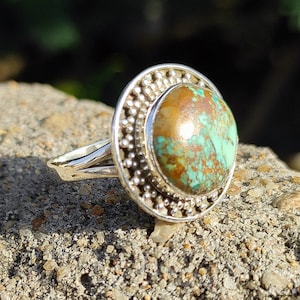 May include: A silver ring with a turquoise stone set in a circular bezel. The bezel is decorated with a row of small beads.