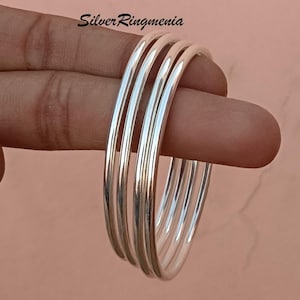 Puede incluir: Cuatro pulseras de plata apiladas. Las pulseras son lisas y brillantes.