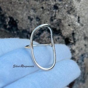 May include: A silver ring with an oval shape. The ring is open and has a smooth, polished finish.