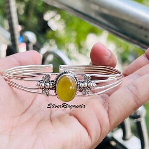 May include: A silver cuff bracelet featuring a central oval yellow gemstone set in a rope-textured bezel. The band consists of four parallel silver wires, with a small silver bee ornament on each side of the stone. The text SilverRingmenia is visible.