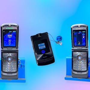 Peut inclure: Trois téléphones portables à clapet Motorola Razr vintage. Deux sont ouverts, affichant un jeu à l'écran, et sont sur des supports bleus. Le troisième téléphone est fermé. Les trois téléphones sont noirs et argentés. Une paire d'écouteurs bleus est attachée au téléphone fermé.