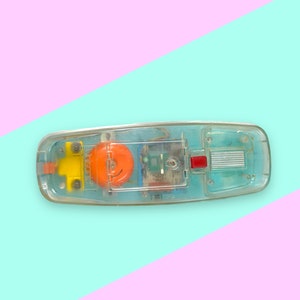 K&ouml;nnte beinhalten: Ein Vintage-Telefon aus klarem Kunststoff mit sichtbaren internen Komponenten. Das Telefon hat ein gelbes und orangefarbenes Design mit dem Aufdruck "Visonic". Das Telefon befindet sich vor einem pastellfarbenen rosa und blauen Hintergrund.
