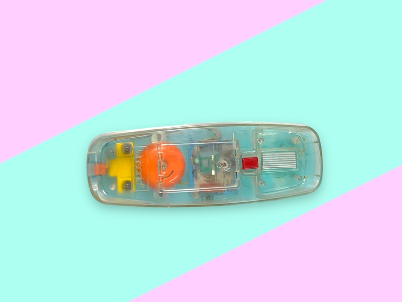 K&ouml;nnte beinhalten: Ein Vintage-Telefon aus klarem Kunststoff mit sichtbaren internen Komponenten. Das Telefon hat ein gelbes und orangefarbenes Design mit dem Aufdruck "Visonic". Das Telefon befindet sich vor einem pastellfarbenen rosa und blauen Hintergrund.