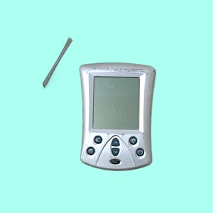 Op de afbeelding: Een zilveren handheld-apparaat met een touchscreen en een stylus. Het apparaat heeft verschillende knoppen onder het scherm en de tekst "MERANGE Touch Screen Databank" boven het scherm. De stylus is grijs.