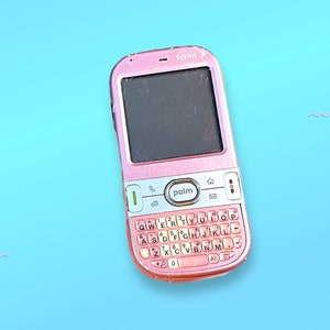 Puede incluir: Un teléfono móvil Sprint Palm rosa con un teclado QWERTY completo y una pantalla pequeña. El teléfono tiene una carcasa rosa y una pantalla negra. La palabra "Sprint" está impresa en la parte superior del teléfono.