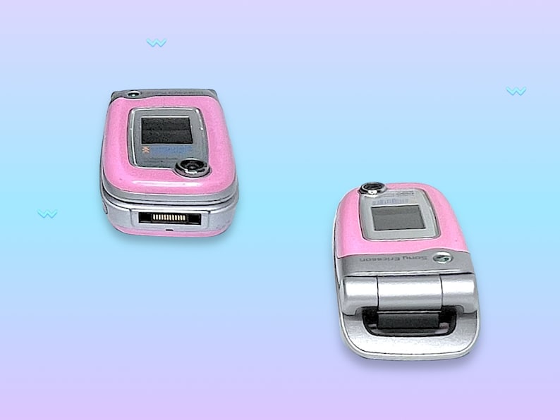 May include: Two pink Sony Ericsson flip phones, one open and one closed, are displayed against a gradient blue and purple background. The phones have silver accents and small screens. The closed phone is on the left, and the open phone is on the right.