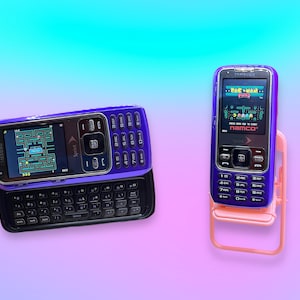 Peut inclure: Deux téléphones portables Samsung vintage. L'un est ouvert, révélant un clavier et un jeu Pac-Man à l'écran. L'autre téléphone est en position verticale dans un support rose, affichant un jeu Namco. Les deux téléphones sont violets et noirs.
