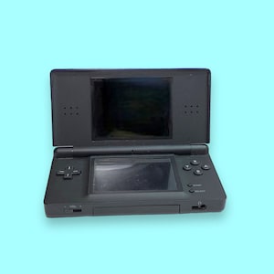 Könnte beinhalten: Eine schwarze Nintendo DS Handheld-Spielkonsole, geöffnet und vor einem hellblauen Hintergrund dargestellt. Die Konsole verfügt über zwei Bildschirme, ein Steuerkreuz und verschiedene Tasten zum Spielen. Die Lautstärkeregelung ist seitlich sichtbar.