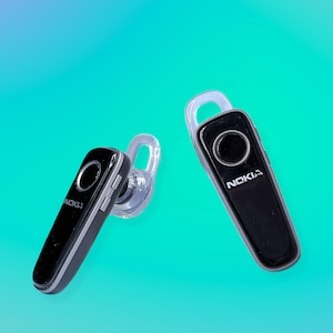 May include: Two black Nokia Bluetooth headsets with silver accents and a clear ear hook are displayed against a teal and blue gradient background. Each headset has a circular button and the Nokia logo.