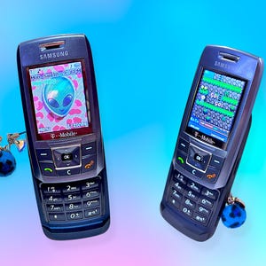 May include: Two dark blue Samsung mobile phones with T-Mobile branding and numeric keypads. The left screen displays an alien graphic with the text Mon, Jan 10, 9:36 PM. The right screen shows a pixelated game. Both phones feature small charms.