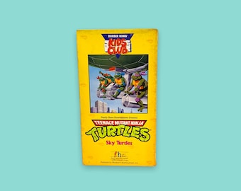 May include: A yellow Burger King Kids Club VHS tape featuring the Teenage Mutant Ninja Turtles. The cover art shows the turtles in a vehicle with a city backdrop. The title "Sky Turtles" is displayed prominently.