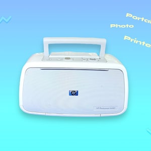 May include: White HP Photosmart A440 portable photo printer with a handle. The printer has a blue HP logo and the words "Portable Photo Printer" are in the background. The printer is on a gradient blue background.