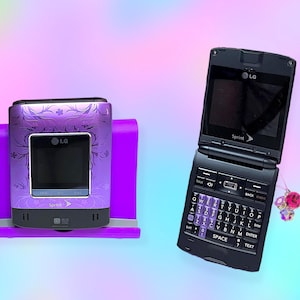 Peut inclure: Deux téléphones portables à clapet LG. L'un est violet avec un motif floral et un écran noir, posé sur un support violet. L'autre est noir, ouvert, avec un clavier et le logo Sprint. Un charme est suspendu au téléphone.