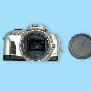 Pode incluir: Corpo de c&acirc;mera Canon EOS IX Lite prateado com uma tampa de lente preta. O corpo da c&acirc;mera tem o logotipo da Canon e "EOS IX Lite" impresso. A tampa da lente tamb&eacute;m tem o logotipo da Canon. Em um fundo azul claro.