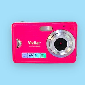 May include: A vibrant pink Vivitar ViviCam 8025 digital camera. It features a silver lens, a flash, and a 2.4-inch LCD monitor. The camera also has a touch screen and 8.1 megapixels.