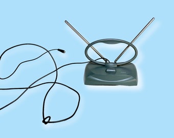 May include: A teal indoor TV antenna with two adjustable metal rods and a circular loop. A black cable extends from the base. The antenna sits on a light blue background.