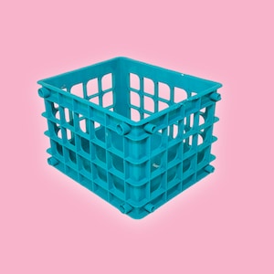May include: A turquoise plastic crate with a grid design. The crate is rectangular with open sides and a solid base. The background is a solid pink colour.