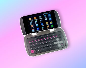 May include: A silver and black smartphone with a slide-out keyboard and a touchscreen display. The screen shows app icons, including Gmail, Facebook, and a calendar. The keyboard has pink accents on the keys. The phone is open, revealing the screen and keyboard.