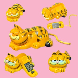 Könnte beinhalten: Eine Sammlung von Vintage-Telefonen in Garfield-Form. Die Telefone sind leuchtend gelb mit schwarzen Streifen und zeigen Garfields Gesicht. Ein Telefon hat einen abgenommenen Hörer und ein Spiralkabel. Der Hintergrund ist einfarbig rosa.
