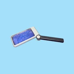 May include: A rectangular magnifying glass with a white frame and a black handle. The lens has a blue, marbled appearance. The handle is connected to the frame with a circular joint. The background is a solid light blue.