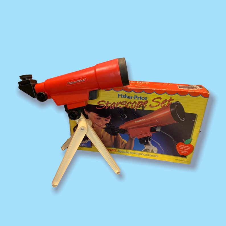 May include: A red Fisher-Price Starscope Set toy telescope with a cream-colored tripod. The box features the words "Starscope Set" and an illustration of a child using the telescope. The telescope is a vintage toy.