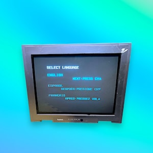 May include: A black computer monitor displays a language selection screen. The text on the screen includes "SELECT LANGUAGE", "ENGLISH", "ESPAÑOL", and "FRANÇAIS", along with instructions to press a button to proceed. The monitor has a dark frame.