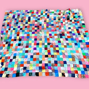 May include: A colorful patchwork quilt composed of numerous fabric squares in various colors and patterns. The quilt features a grid-like design with squares of red, blue, green, yellow, and more. The quilt is a large size, suitable for a bed.