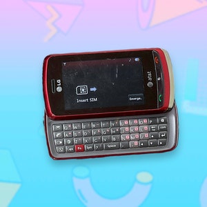 Peut inclure: Un téléphone portable LG rouge avec un clavier coulissant, avec le logo AT&T. L'écran affiche "Insert SIM" et "Emerge". Le téléphone est ouvert, révélant un clavier complet QWERTY.