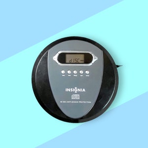 May include: A black and grey Insignia portable CD player with a digital display and control buttons. The device has the text "INSIGNIA" and "60 SEC ANTI-SHOCK PROTECTION" printed on it. The CD player is on a blue and light blue background.
