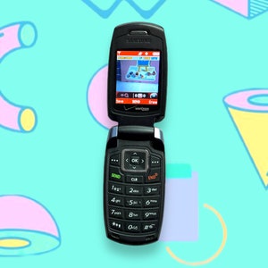May include: Black Samsung flip phone, open to reveal a screen displaying a game. The phone has a keypad with numbers and function keys. The background is a light blue with colorful geometric shapes.