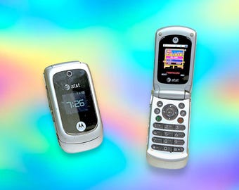 May include: Two silver flip phones are displayed against a colorful, iridescent background. One phone is closed, displaying the time 7:26 and the AT&T logo. The other phone is open, showing a game screen and the AT&T logo.