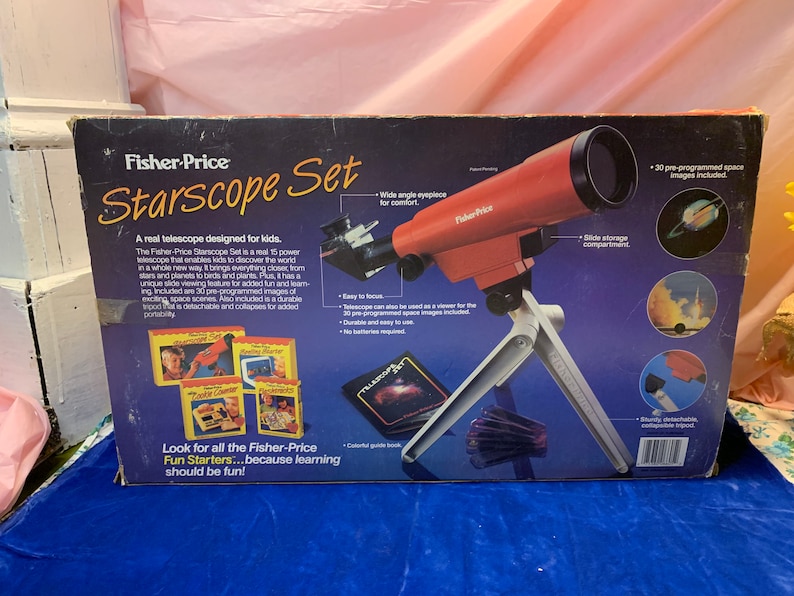 May include: A Fisher-Price Starscope Set, a real telescope for kids, is displayed. The red telescope sits on a white tripod. The box features the product name, images of space, and text that reads "Look for all the Fisher-Price Fun Starters...because learning should be fun!"