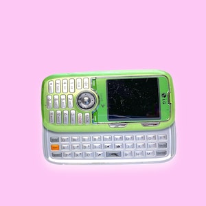 Peut inclure: Un téléphone portable LG Sprint vert avec un clavier coulissant, sur fond rose. Le téléphone possède un pavé numérique et un écran avec des rayures visibles. Le clavier est argenté et blanc.