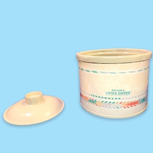 May include: A cream-colored Rival Little Dipper slow cooker with a matching lid. The slow cooker has a decorative band with geometric patterns in teal, orange, and green. The text "RIVAL LITTLE DIPPER" is printed on the front.