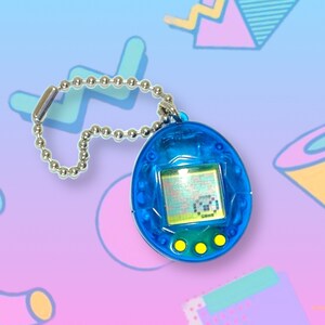 May include: A blue handheld digital pet game with a silver chain. The egg-shaped device has a small screen displaying pixelated graphics and three yellow buttons below. The background features a colorful, retro-style design.