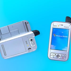 May include: Two silver Sprint Pocket PC devices on a blue background. One device is open, revealing its interior. The other device displays a Windows Mobile screen. Both devices have a camera and a black antenna.