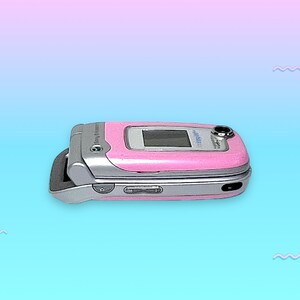 May include: A pink and silver clamshell cell phone. The phone is open, revealing a small screen. The phone has a silver hinge and a pink exterior. The phone is a vintage model.