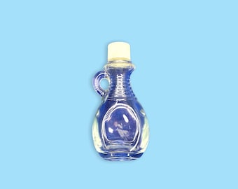 May include: A clear glass syrup bottle with a white cap and a small handle. The bottle has a ridged design and is empty. The background is a solid light blue.