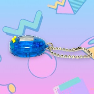 May include: A blue handheld digital pet toy with a silver chain. The toy has a small screen and yellow buttons. The background is a colorful, abstract design with geometric shapes in shades of blue, pink, and purple.