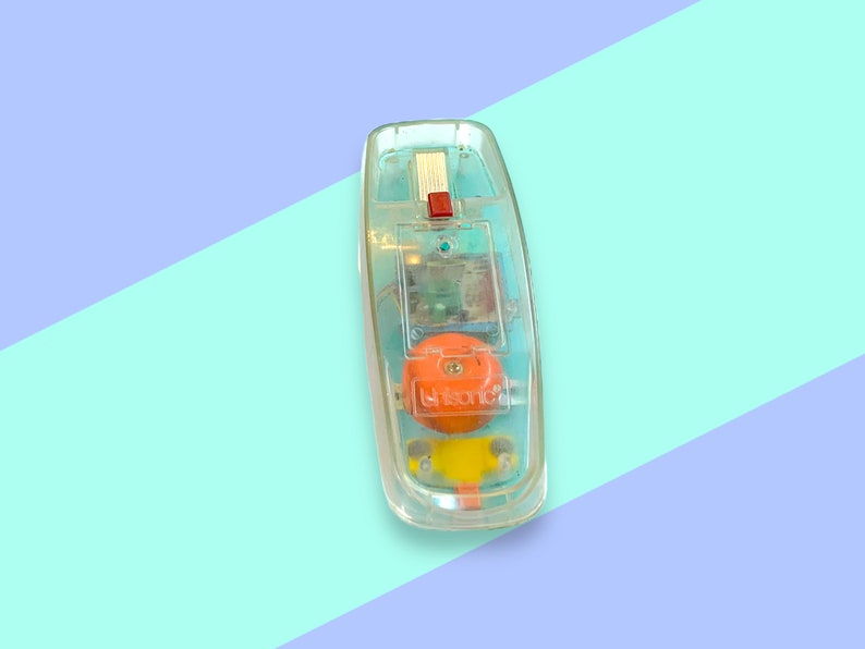K&ouml;nnte beinhalten: Ein Vintage-Spielzeugtelefon aus klarem Kunststoff mit einem orangefarbenen Zifferblatt und einer roten Taste. Die internen Komponenten des Telefons sind sichtbar. Der Hintergrund ist hellblau und lila geteilt.
