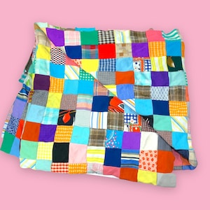 May include: A colorful patchwork quilt with a variety of fabric squares in shades of blue, green, yellow, red, and purple. The quilt is folded, showcasing the different patterns and textures of the fabric. A handmade, vintage textile.
