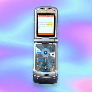 Peut inclure: Téléphone portable Motorola argenté à clapet, affichant "Enter Unlock Code" sur l'écran. Le téléphone a un clavier avec des accents bleus et un bouton de navigation central. Le téléphone est ouvert.