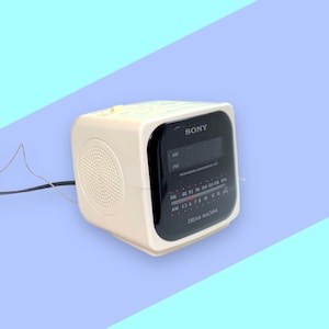 May include: Cream-colored Sony Dream Machine AM/FM clock radio. The radio has a digital display, a speaker, and a tuning dial. The text "SONY" is visible on the top left of the display. The radio is on a blue and purple background.