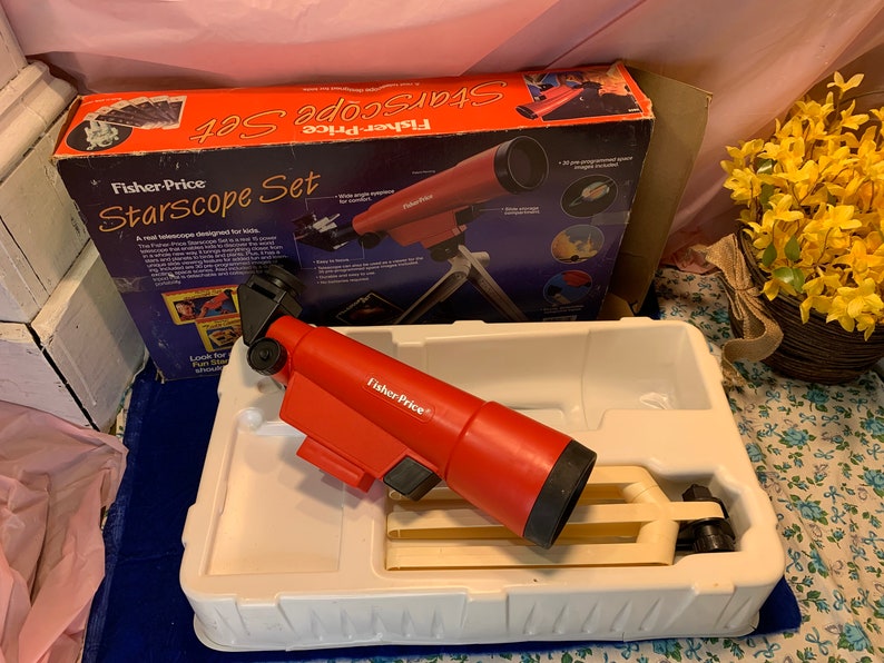 May include: A red Fisher-Price Starscope Set, designed for kids, is displayed in its original box and packaging. The telescope is red with black accents and sits in a white plastic tray. The box features images of space and the words "Starscope Set".
