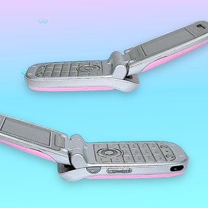 May include: Two silver flip phones with pink accents are displayed against a gradient blue and pink background. The phones are open, revealing the keypad and screen. The design is a retro style.