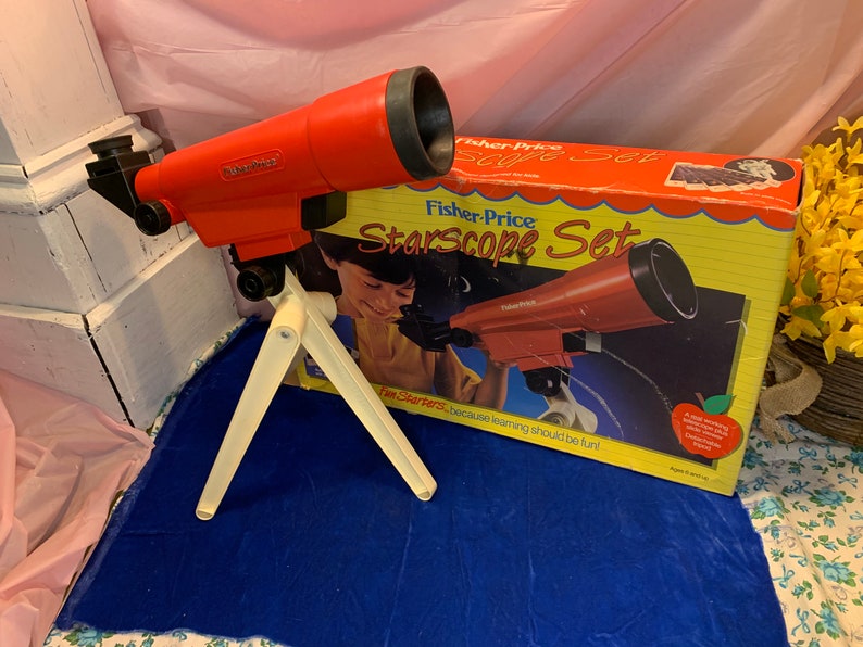 May include: A red Fisher-Price Starscope Set toy telescope with a white tripod, and a box with the same telescope image. The box reads "Starscope Set" and "Fun Starters because learning should be fun!"