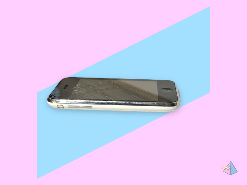 May include: A damaged, silver and white smartphone with a cracked screen. The phone is lying on a diagonal blue and pink background. The screen is black, and the phone has a silver border.