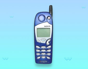 May include: A blue Nokia cell phone with a silver screen and a black antenna. The phone has a keypad with white numbers and the Cingular logo at the bottom. The word "NOKIA" is printed above the screen.