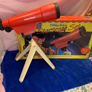 May include: A red Fisher-Price Starscope toy telescope with a cream-colored tripod, and a box with the same telescope image. The box reads "Starscope Set" and "because learning should be fun!"