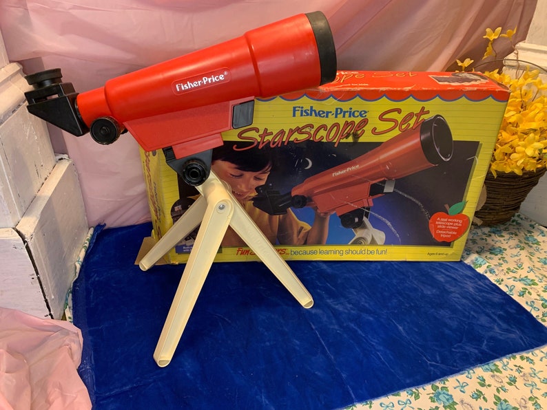 May include: A red Fisher-Price Starscope toy telescope with a cream-colored tripod, and a box with the same telescope image. The box reads "Starscope Set" and "because learning should be fun!"